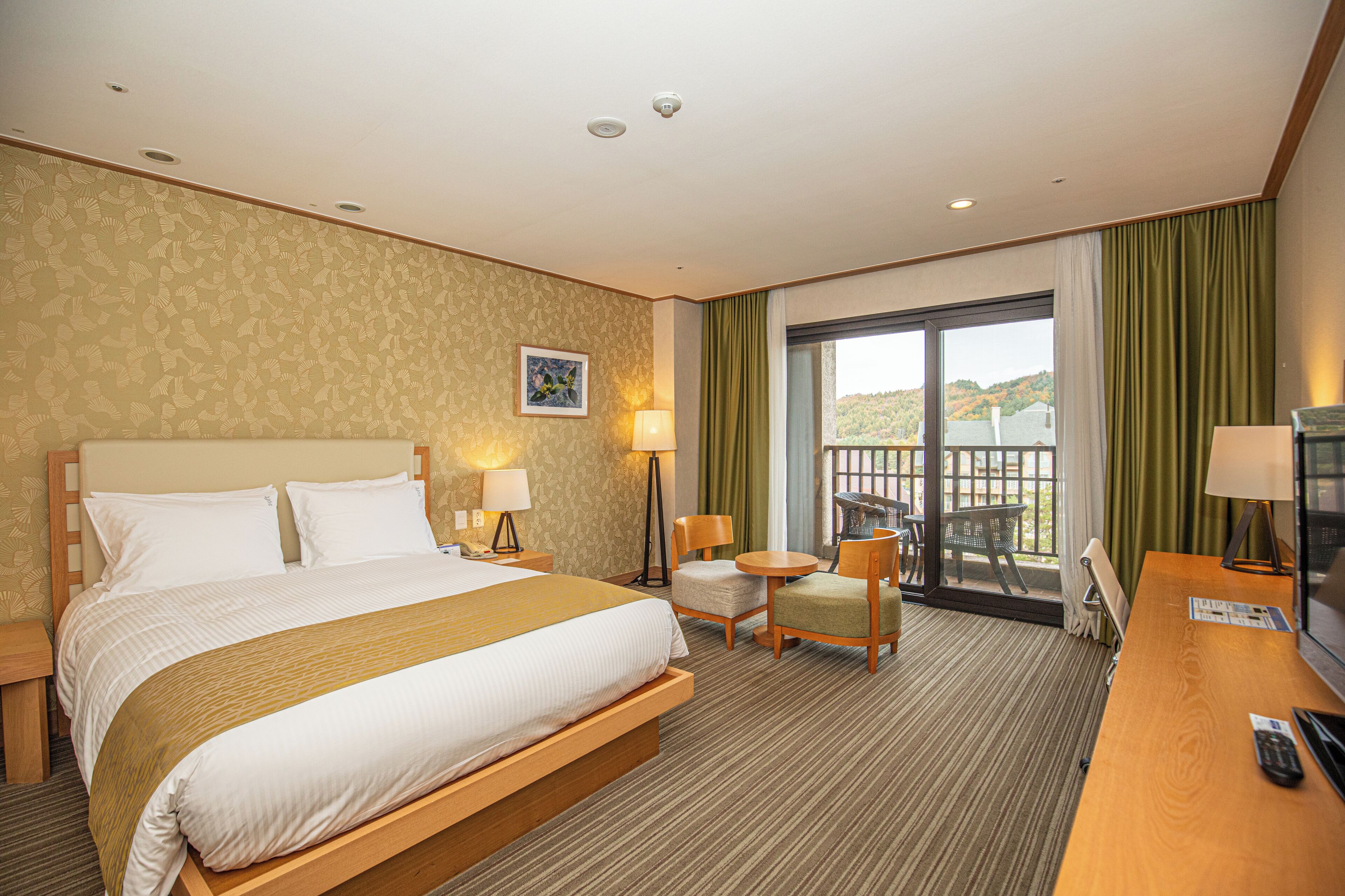 Ein Hotelzimmer mit einem großen Bett, zwei Stühlen, einem Schreibtisch mit Fernseher und einem Balkon mit Blick.