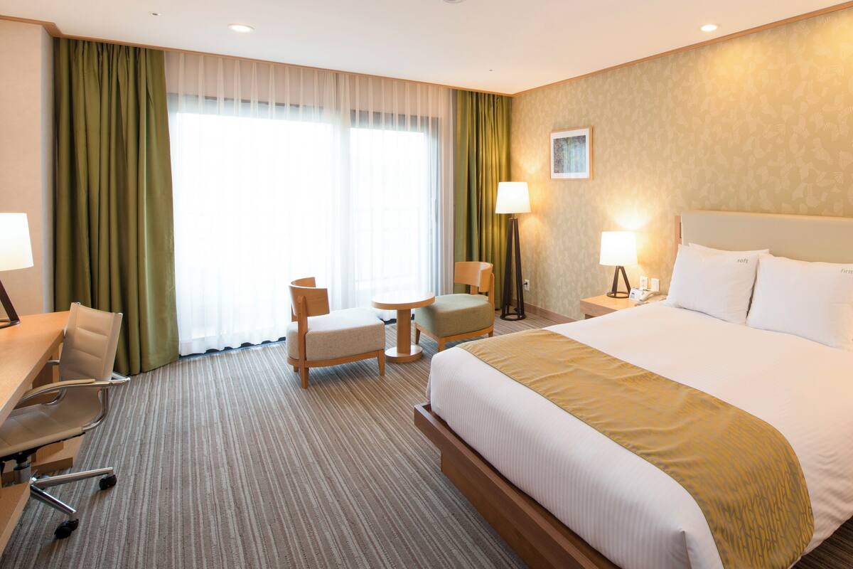 Une chambre d’hôtel avec un grand lit, un bureau, deux chaises, une petite table et une lampe.