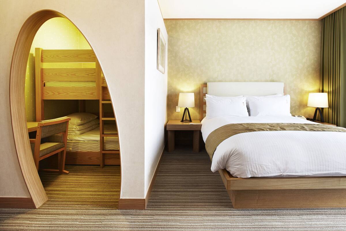 Une chambre d’hôtel avec un lit superposé, un lit simple, deux lampes de chevet, une table de chevet et un sol recouvert de moquette.
