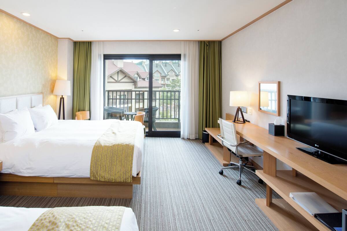 Une chambre d’hôtel avec un lit, un bureau, une télévision et un balcon offrant une vue.