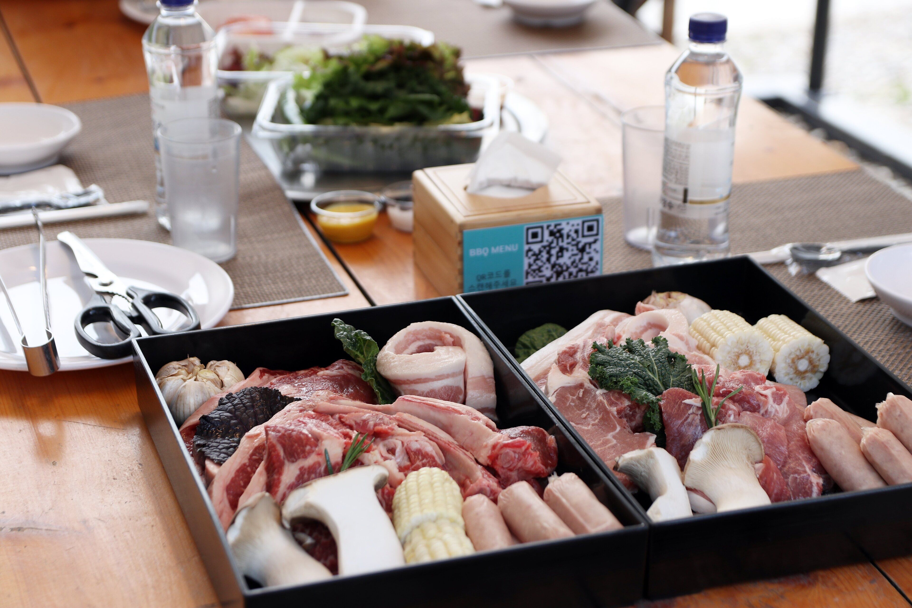A meal tray with various meats and vegetables, a QR code, and a water bottle on a table.