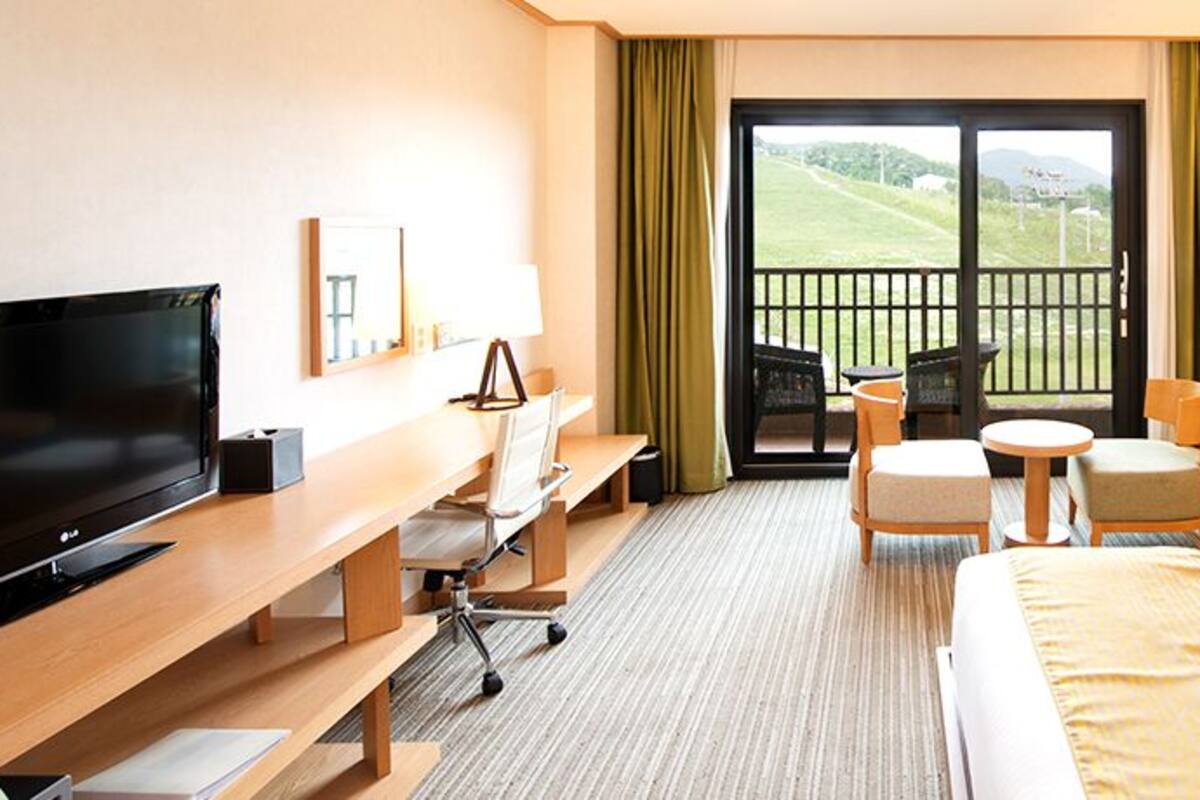 Une chambre d’hôtel équipée d’un lit, d’une télévision, d’un bureau, d’une chaise, d’une petite table et d’un balcon donnant sur l’extérieur.