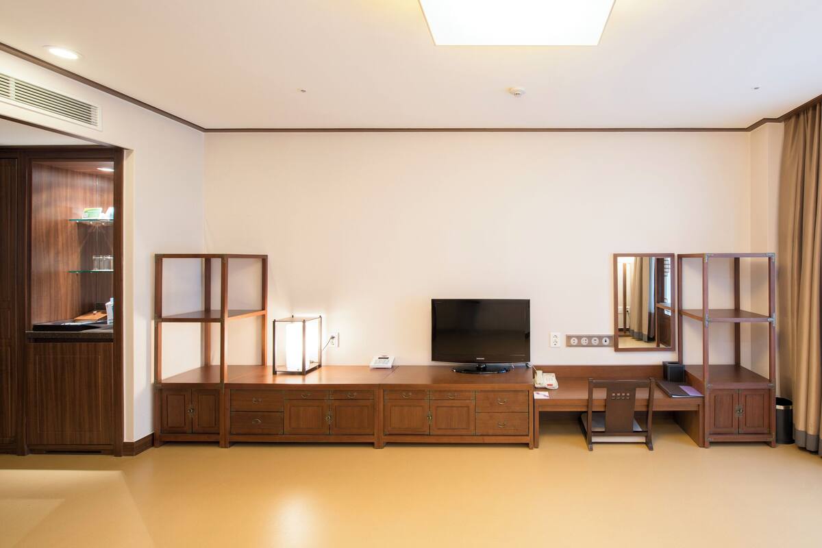 Une chambre d’hôtel avec un bureau en bois, une télévision et une grande fenêtre avec des rideaux.