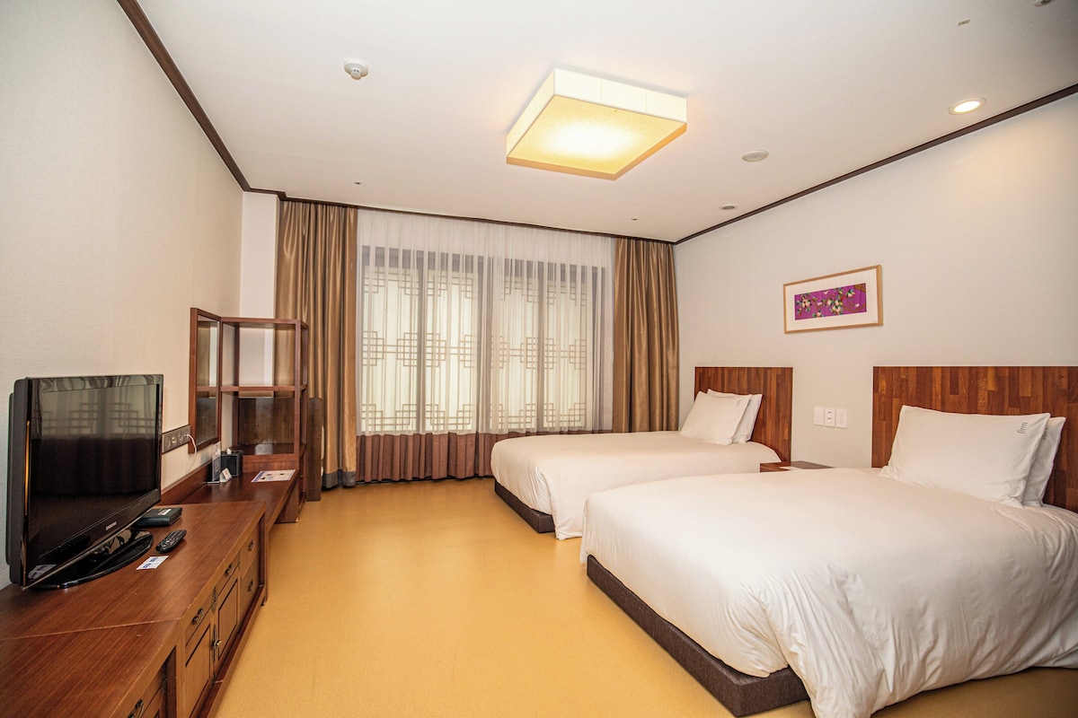 Een hotelkamer met twee bedden, een televisie op een houten kast en een groot raam met gordijnen.