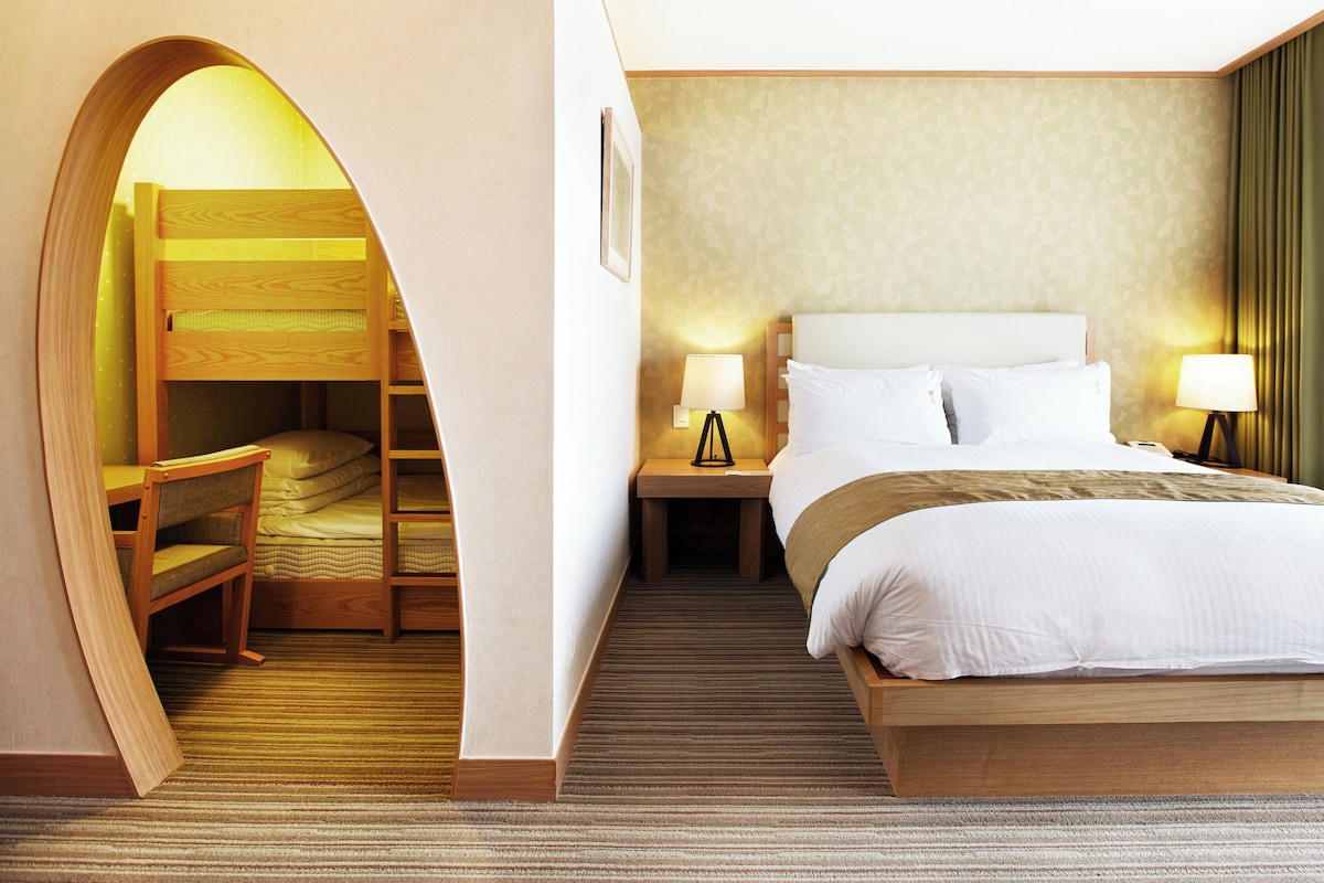 Een hotelkamer met een stapelbed, een eenpersoonsbed, twee bedlampen, een nachtkastje en een vloerbedekking.