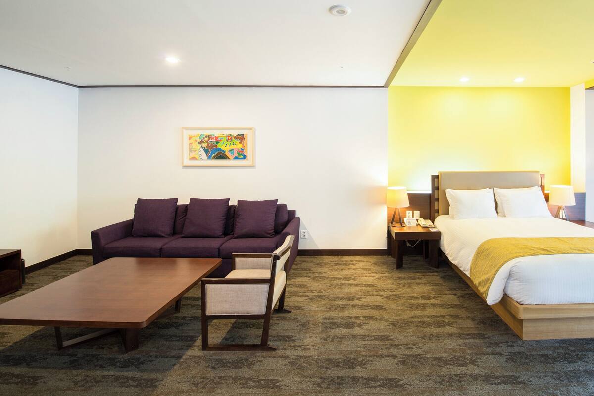 Une chambre d’hôtel comprenant un lit, un canapé, une table basse et une table de chevet avec une lampe.