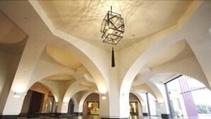 Un interior espacioso con techos altos y puertas en arco, que incluye un candelabro geométrico y un suelo pulido.