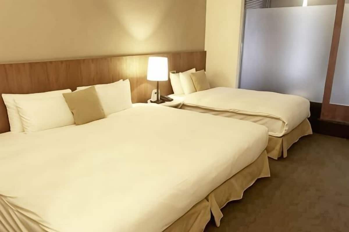 Ein Hotelzimmer mit zwei Betten, einem Nachttisch mit Lampe und einem Fenster mit Blick.