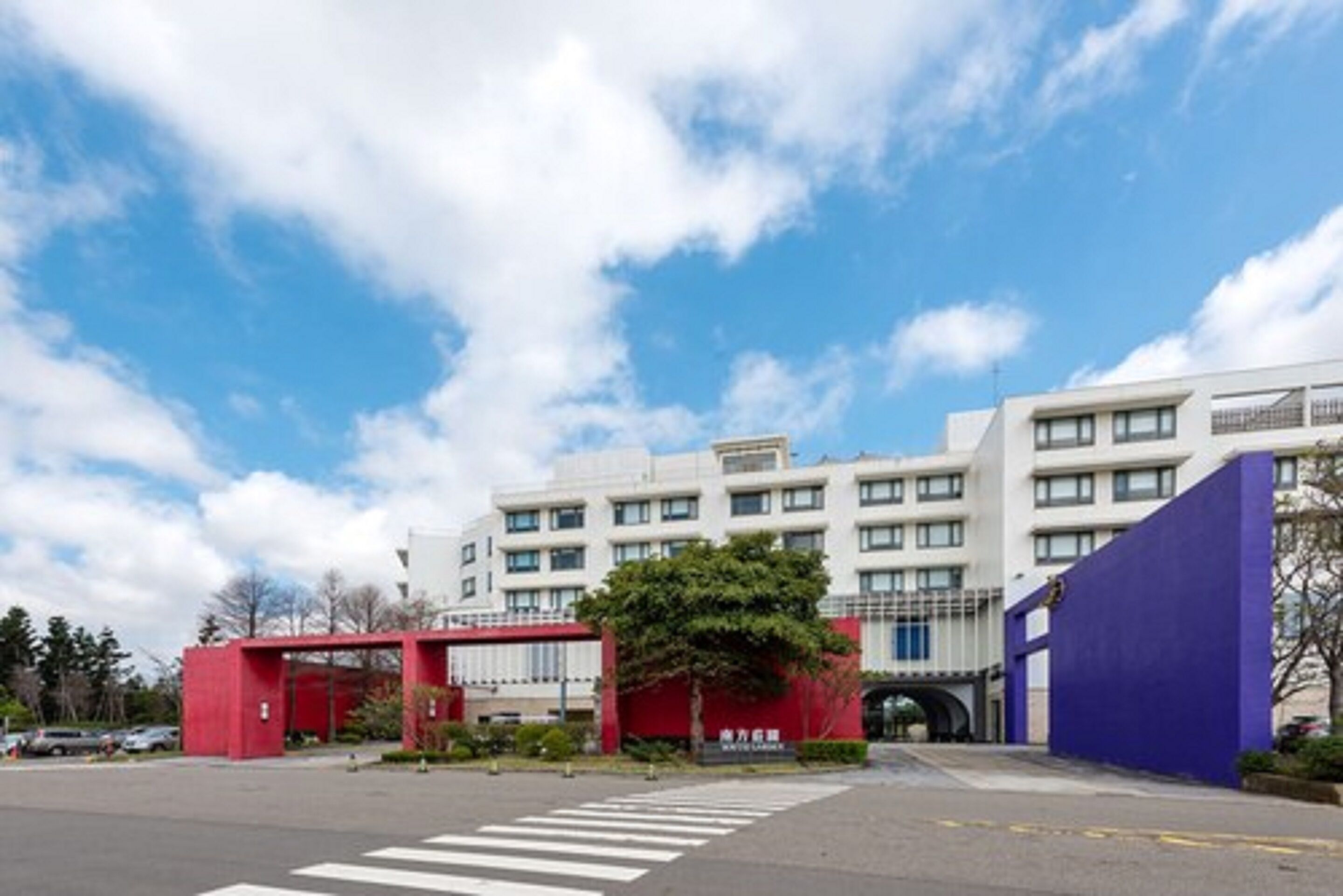 A modern building with a red entrance gate, a parking lot, and a clear blue sky.
