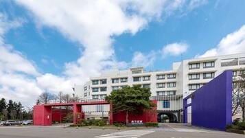 A modern building with a red entrance gate, a parking lot, and a clear blue sky.