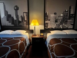 Habitación de hotel con dos camas, una mesita de noche con lámpara y vistas a la ciudad.