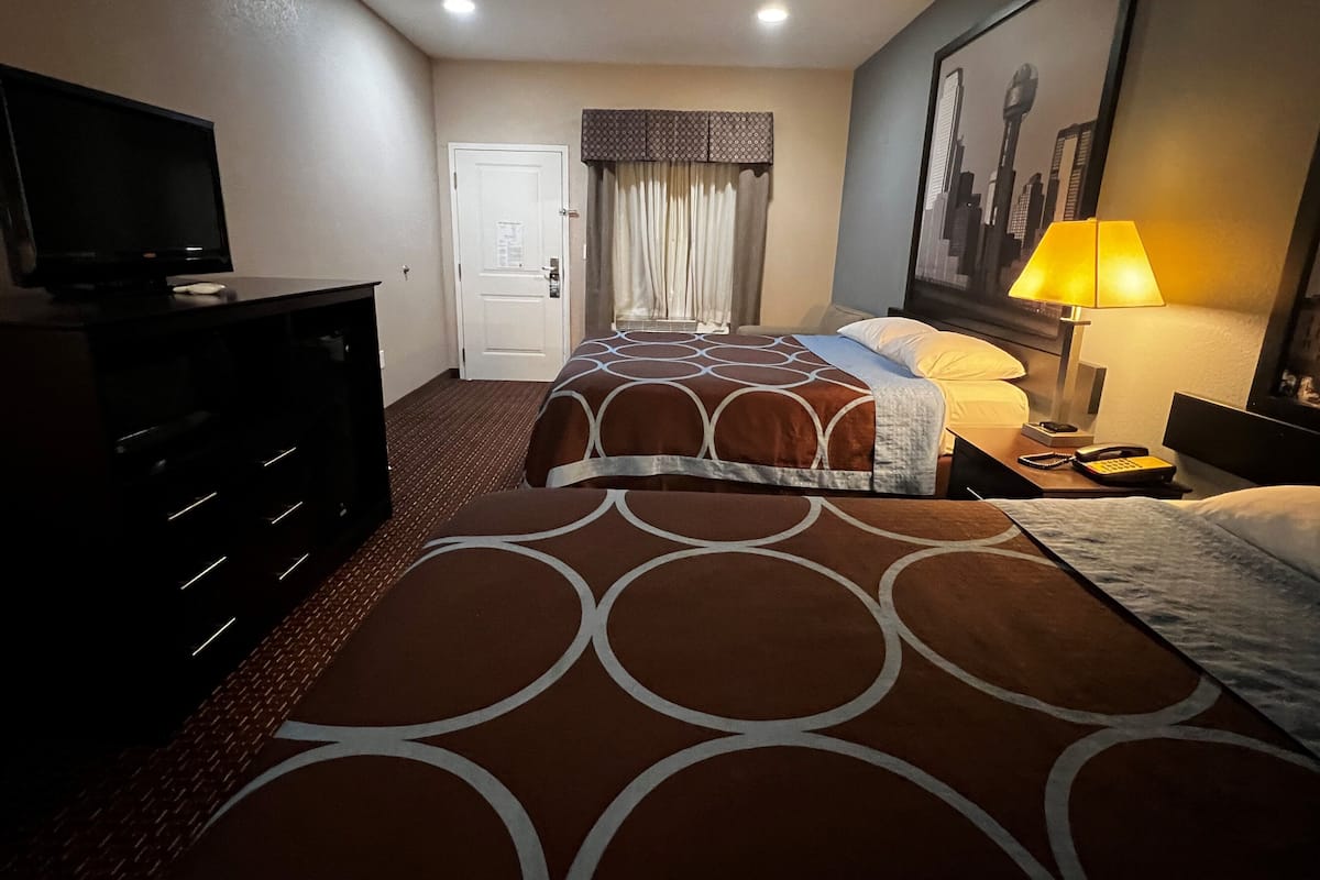 A hotel room with two beds, a TV, a desk with a lamp, and a painting on the wall.