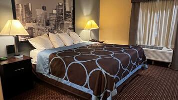 A hotel room with a bed, two bedside lamps, a cityscape wall art, a window with curtains, and an air conditioning unit.