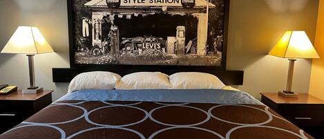 A hotel room with a bed, two bedside lamps, a telephone, and a poster of a vintage Coca-Cola truck on the wall.