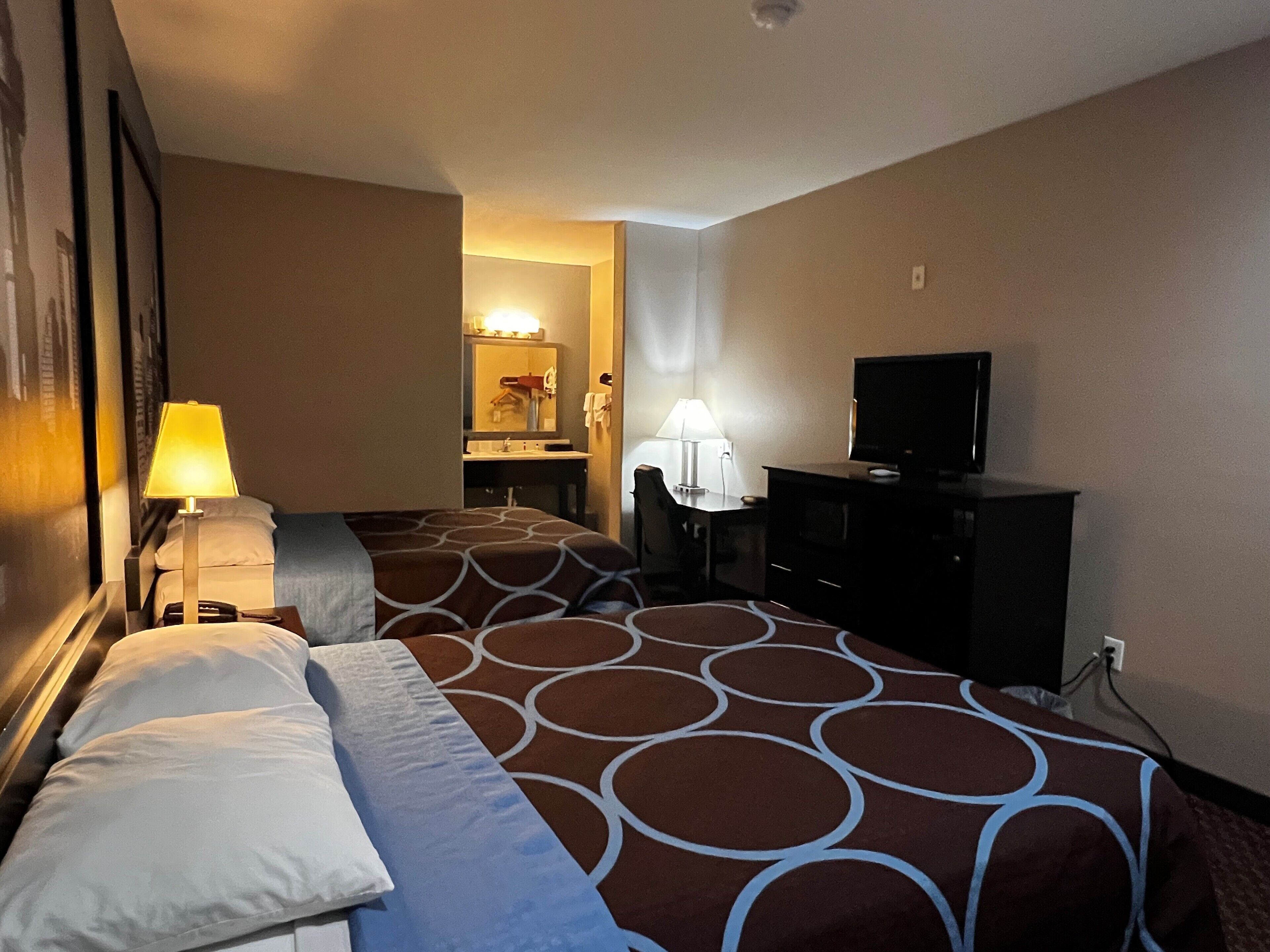 A hotel room with two beds, a desk, a television, and a bathroom visible through an open door.