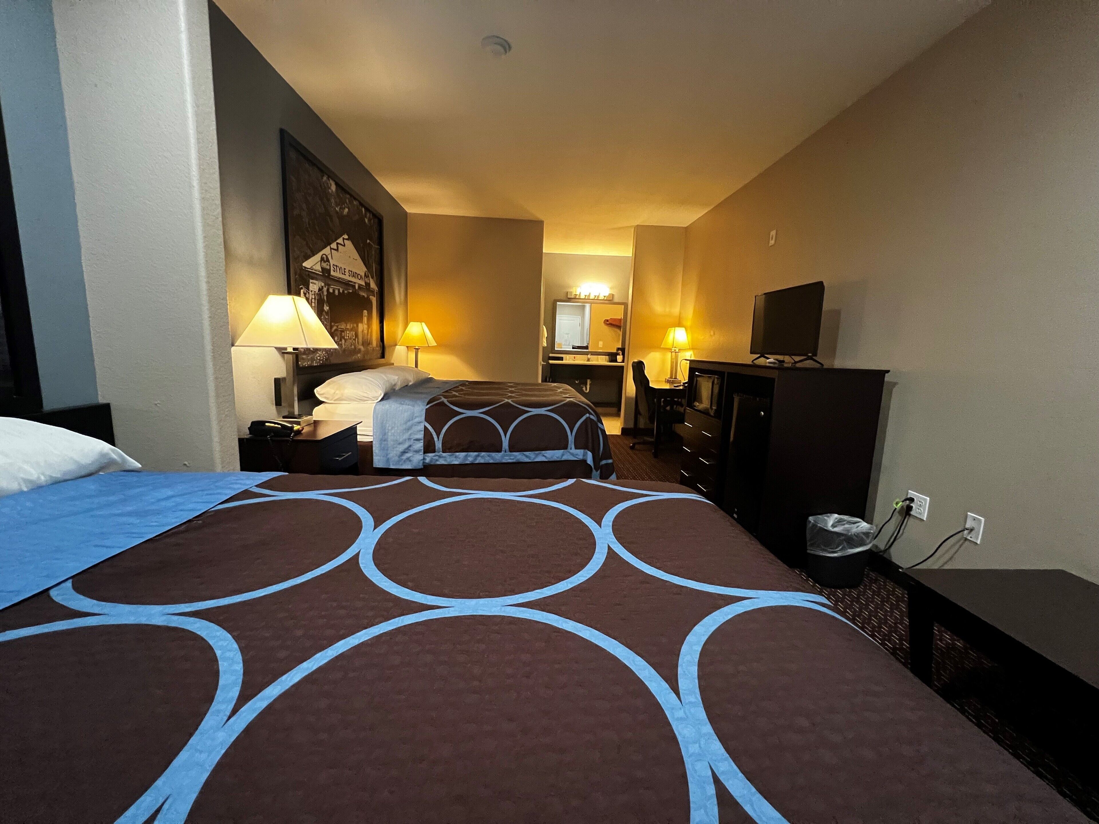 A hotel room with a bed, a desk, a chair, a television, and a lamp.