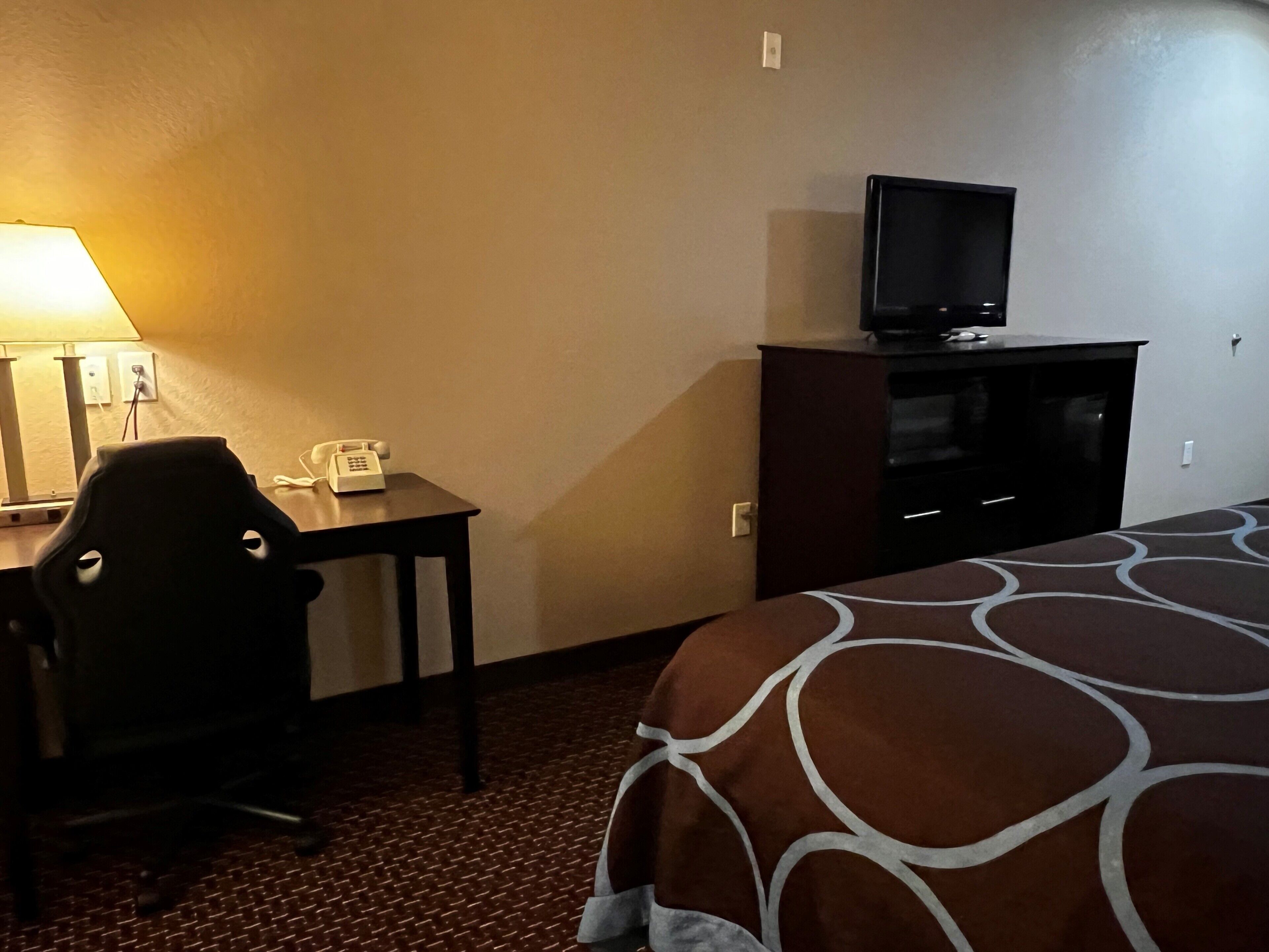 A hotel room with a bed, a desk with a telephone, a chair, a television on a cabinet, and a lamp.