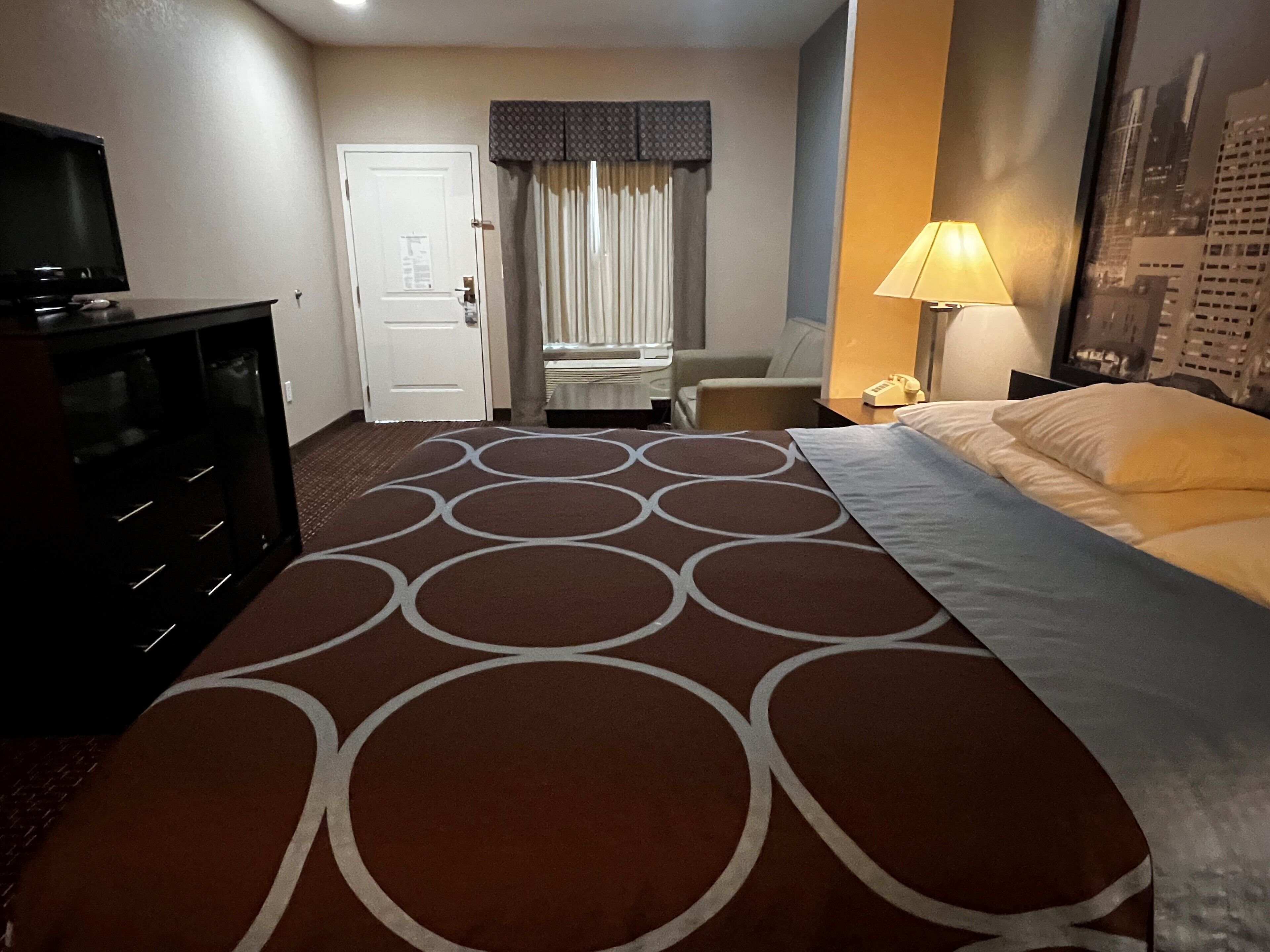 A hotel room with a bed, a desk, a chair, a TV, and a lamp.