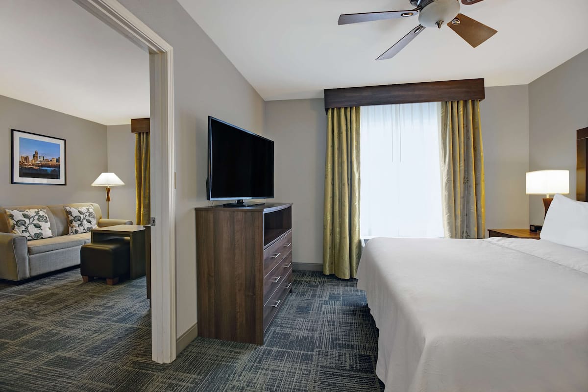 A hotel room with a bed, a TV, a sofa, a desk, and a window with curtains.