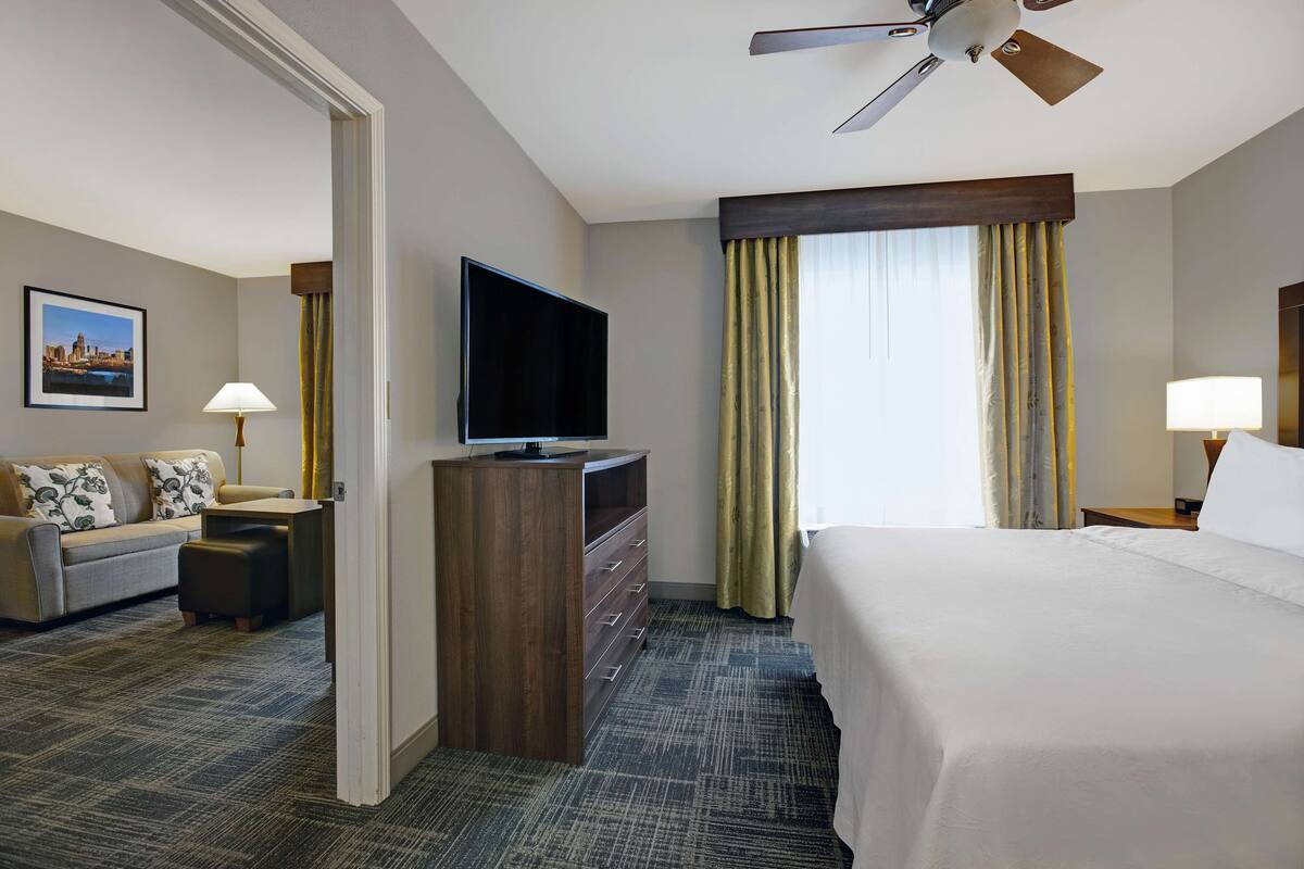 A hotel room with a bed, a TV, a sofa, a desk, and a window with curtains.