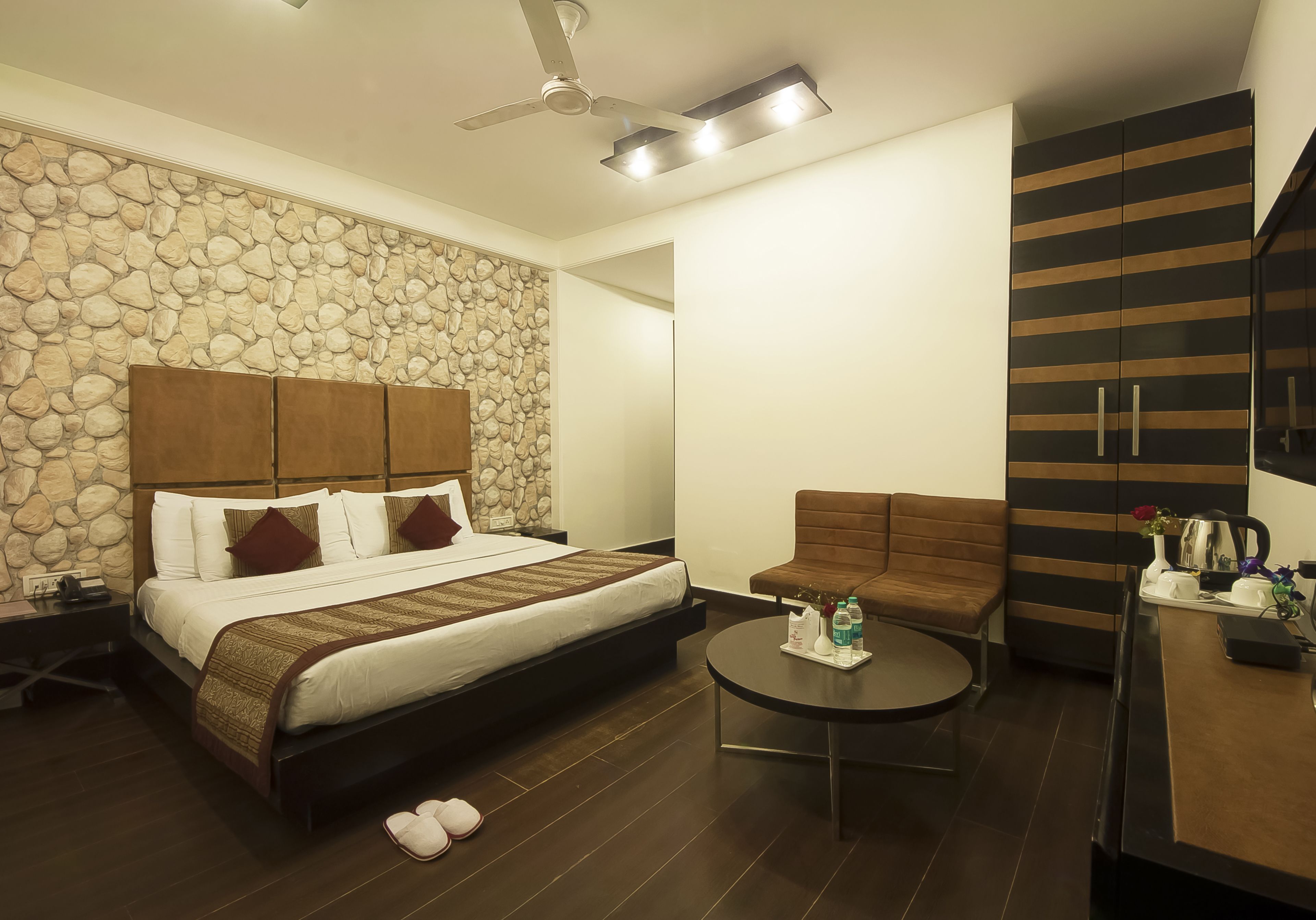 Una habitación de hotel con pared de piedra, una cama con cabecera de madera, un sofá marrón, una mesita de centro redonda y un armario a rayas horizontales.