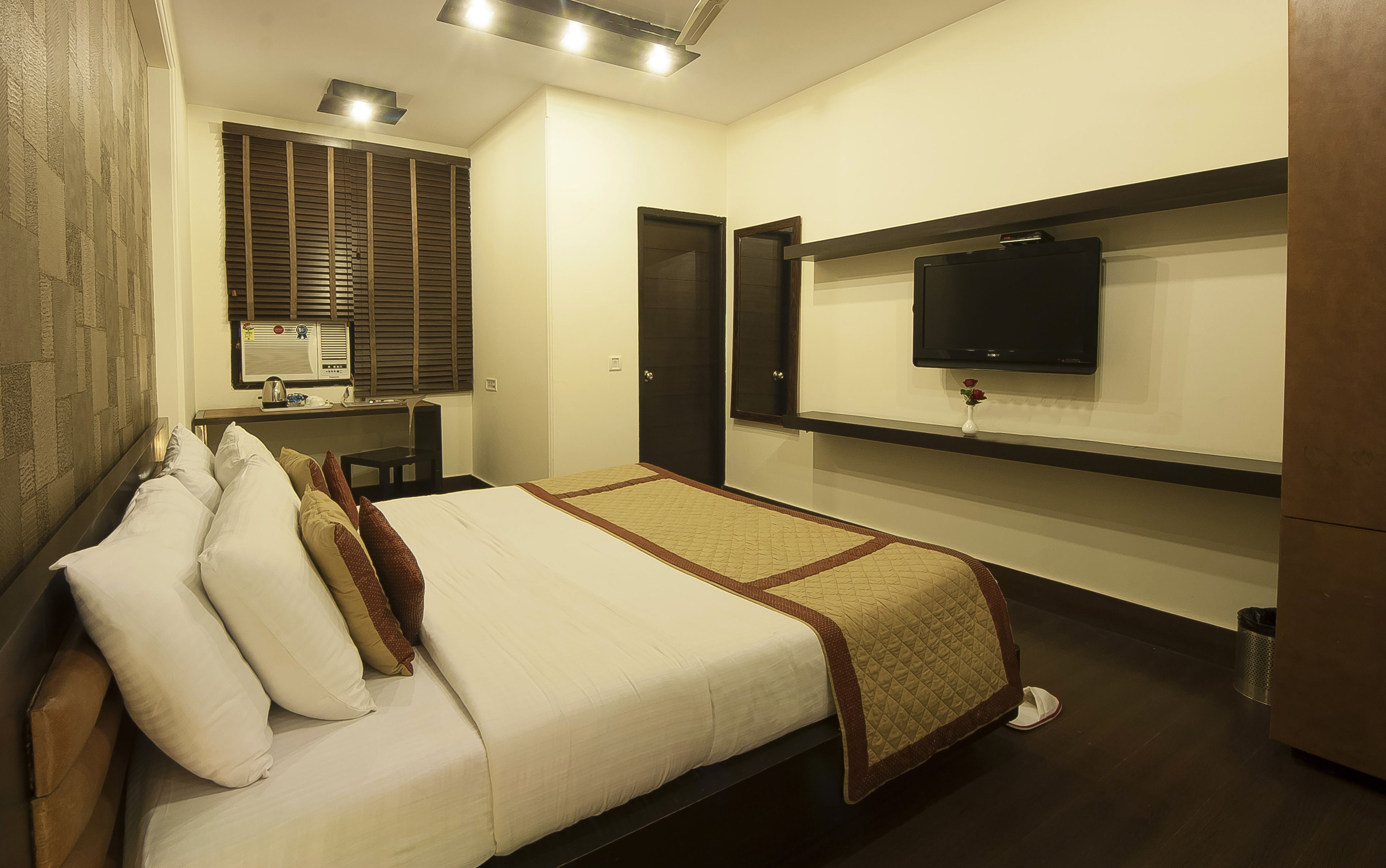 A hotel room with a bed, a desk, a television, and a window with blinds.