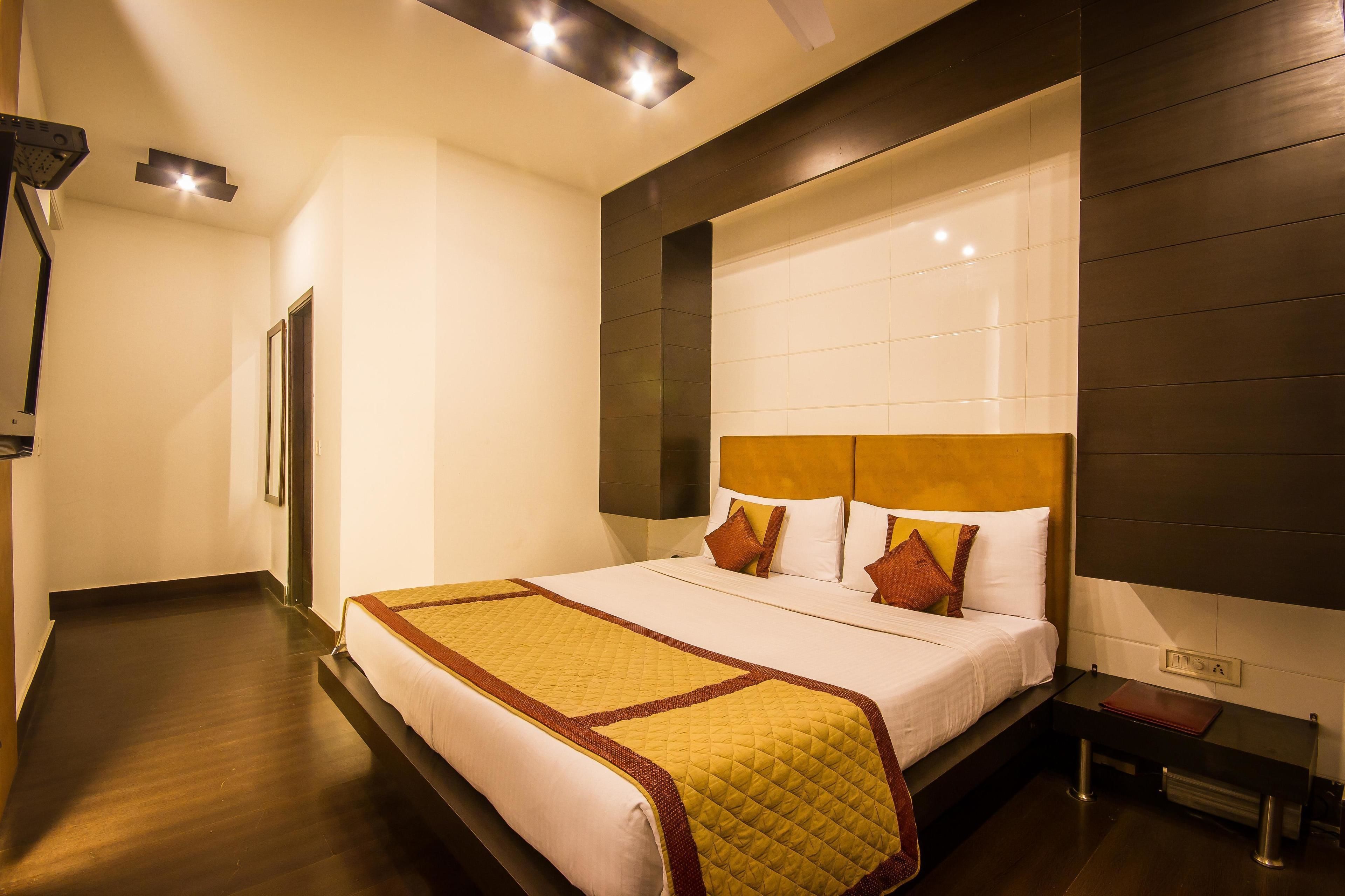 A hotel room with a large bed, a bedside table, a nightstand, and a wall-mounted TV.