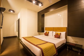 A hotel room with a large bed, a bedside table, a nightstand, and a wall-mounted TV. - Hotel Good Palace (New Delhi)