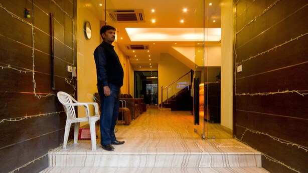 Un hombre de pie en una escalera con diseño interior moderno, incluyendo un piso estampado y una puerta de cristal que da a otra área.