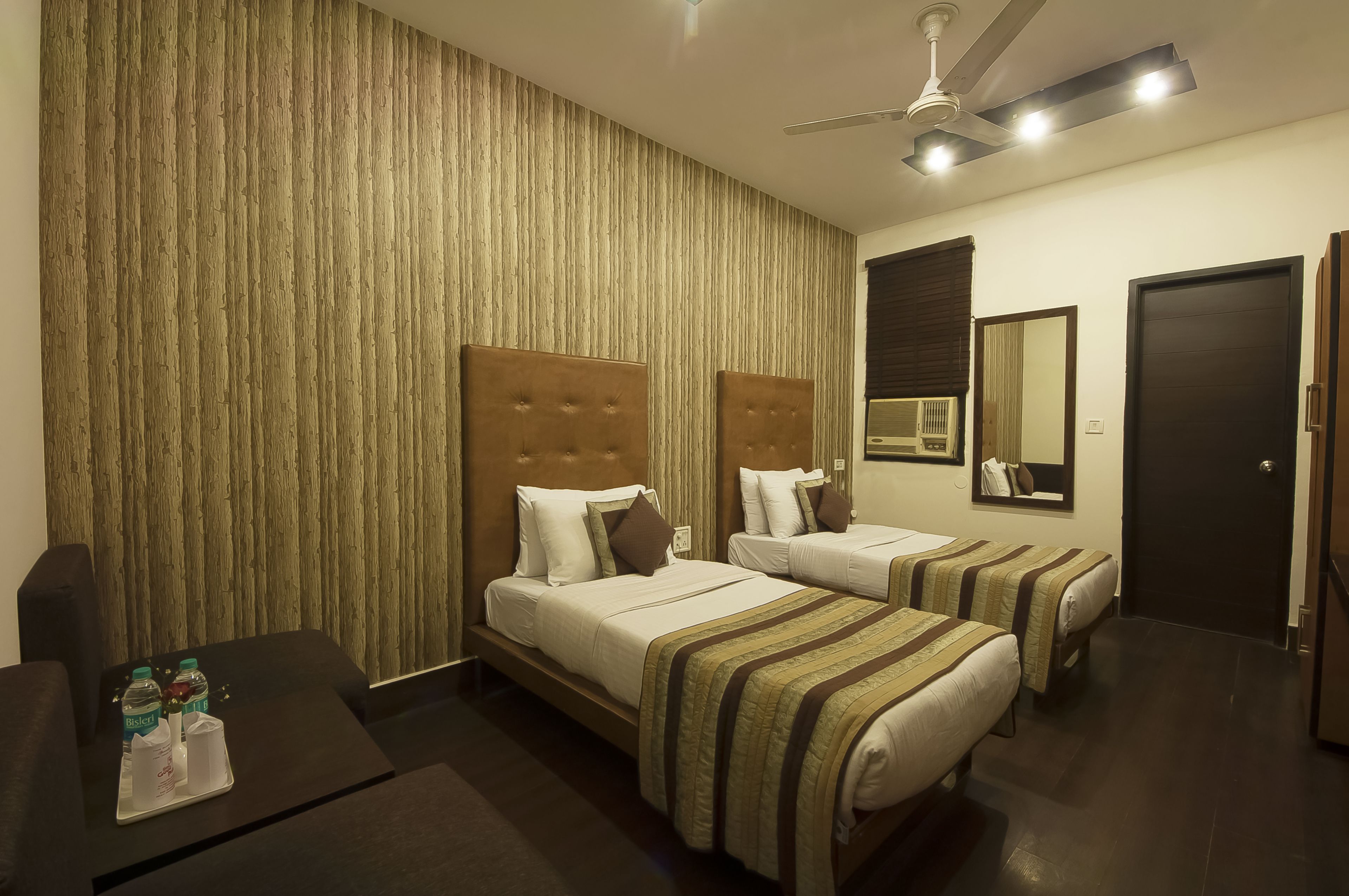 A hotel room with two beds, a desk with a tray of water bottles, and a ceiling fan.