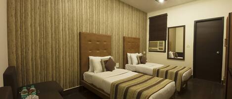 A hotel room with two beds, a desk with a tray of water bottles, and a ceiling fan.