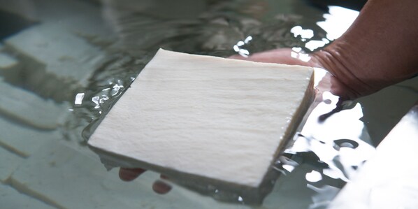 Une main tenant un objet rectangulaire blanc au-dessus de l’eau.
