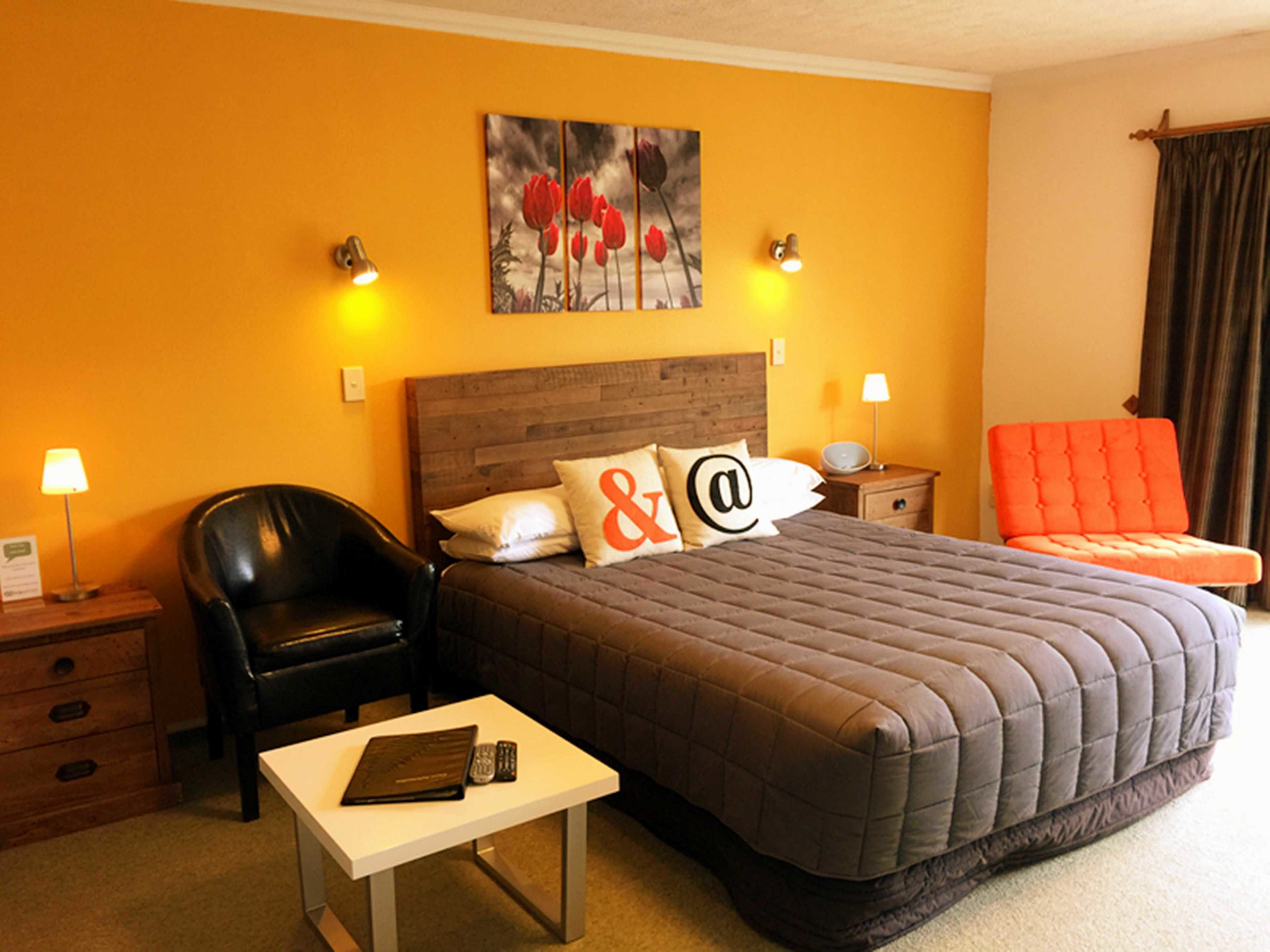 A hotel room with a large bed, a desk, a chair, and a nightstand with lamps.