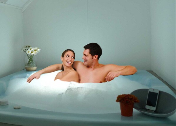 A couple in a bathtub with a smartphone and a flower vase on the side. - Rotorua Coachman SPA Motel (Rotorua)