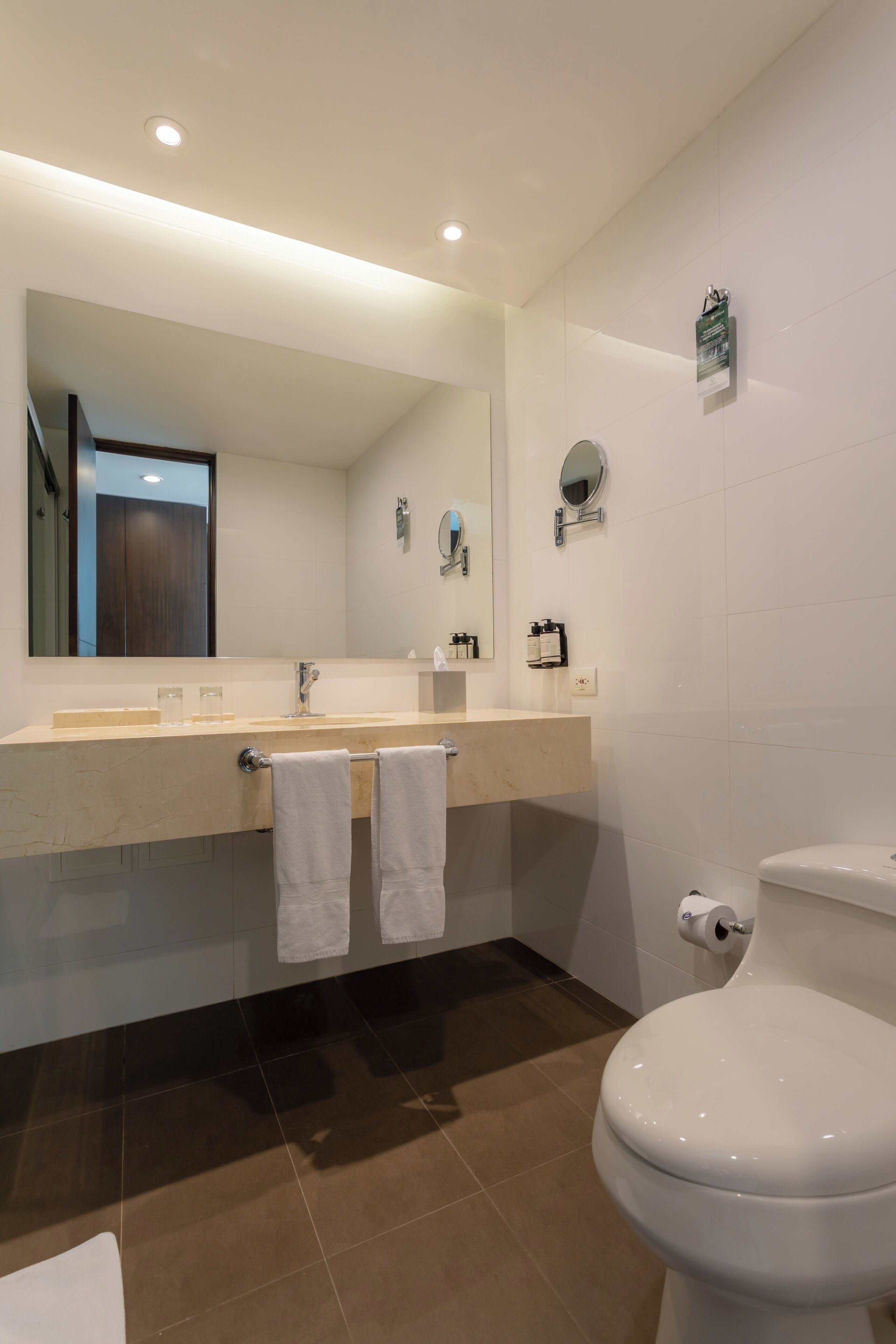 Een moderne badkamer met een grote spiegel, een wastafel, twee handdoeken, een toilet en een douchehoek.