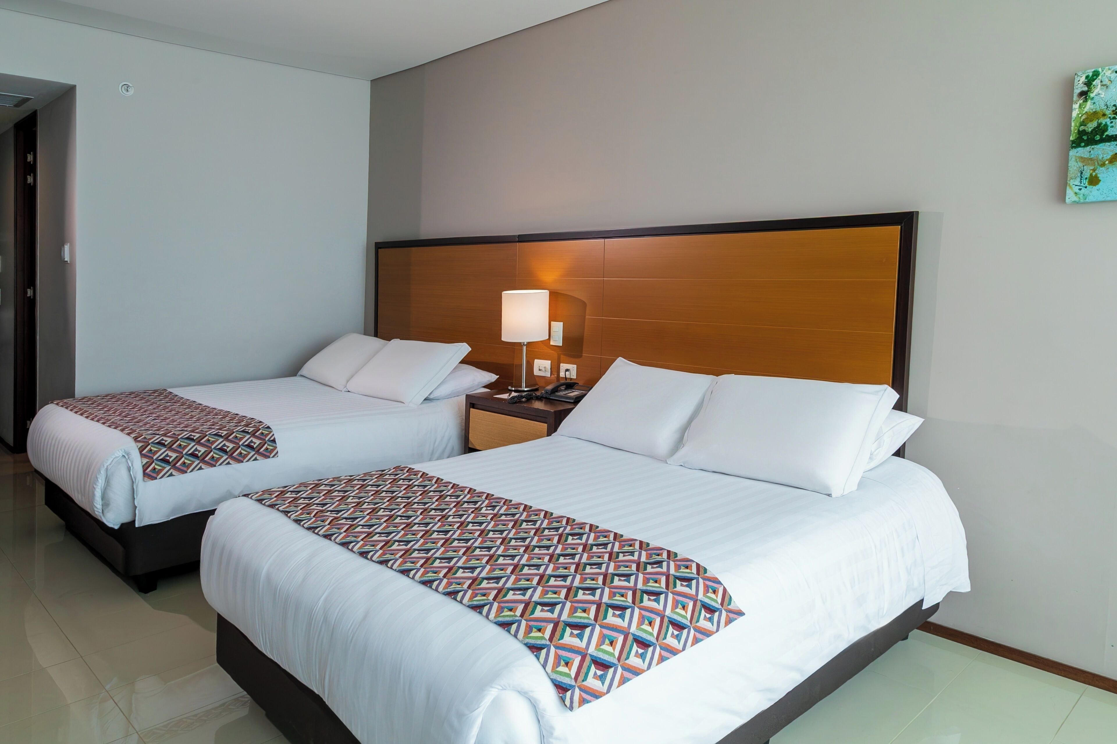 A hotel room with two beds, a nightstand with a lamp, and a wooden headboard.