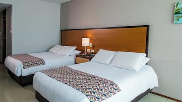 Habitación de hotel con dos camas, una mesita de noche con lámpara y cabecero de madera.