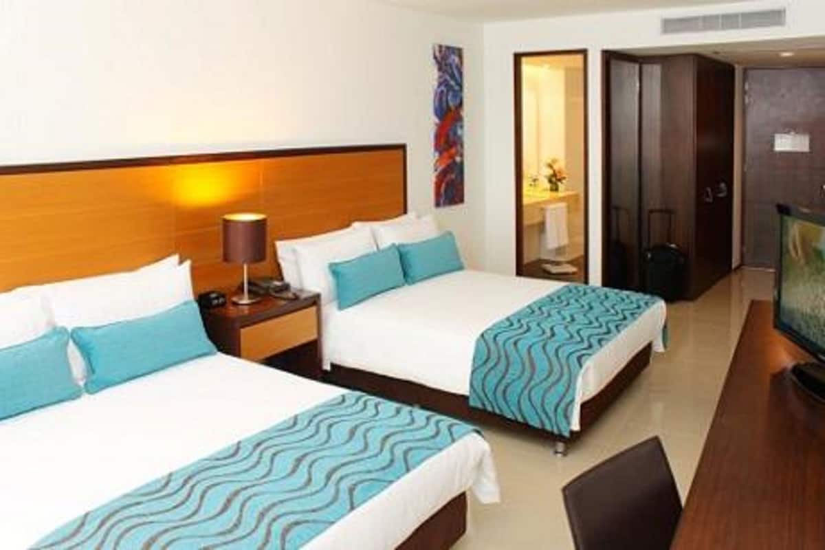 Een hotelkamer met twee bedden, een nachtkastje, een televisie en een deur die naar een andere kamer leidt.
