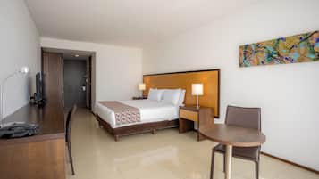 Habitación de hotel con cama, mesita de noche, lámpara, escritorio, silla y un cuadro en la pared.