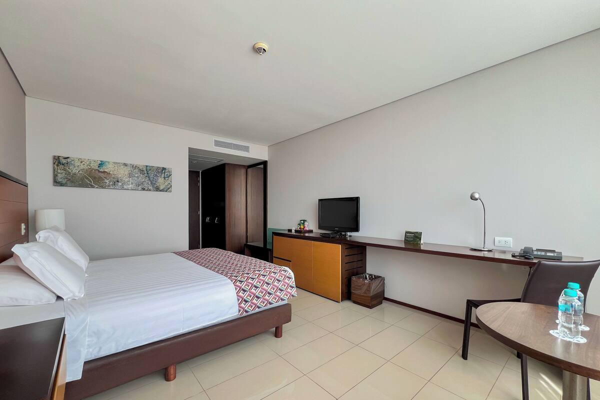 Een hotelkamer met een bed, bureau, televisie, stoel en een klein tafeltje met een waterfles.