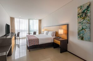 A hotel room with a bed, bedside table, lamp, TV, desk, chair, and a large abstract painting on the wall. - Hotel Estelar En Alto Prado (Barranquilla)