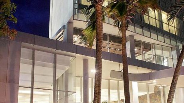 Un edificio moderno con ampie vetrate, palme e una scalinata che conduce a un piano superiore.