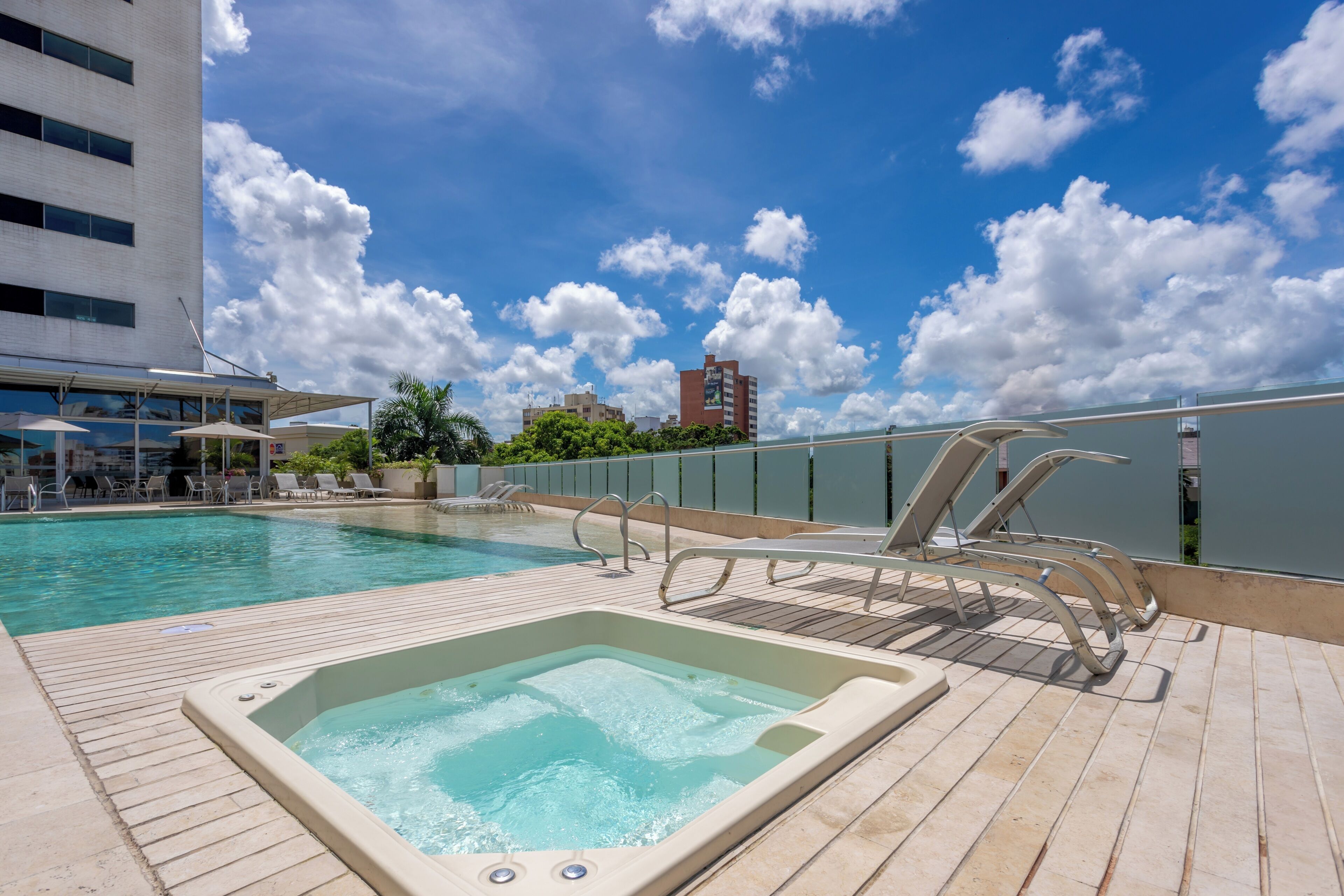 Une piscine sur le toit, avec un jacuzzi, des chaises longues et une vue sur les toits de la ville.