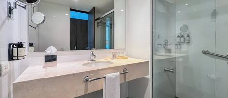 Un baño moderno con un espejo grande, dos lavamanos, cabina de ducha con mampara de vidrio y un perchero para toallas.