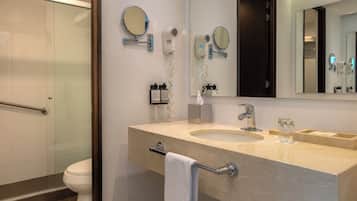 Un baño moderno con cabina de ducha de vidrio, un espejo grande y tocador con perchero.