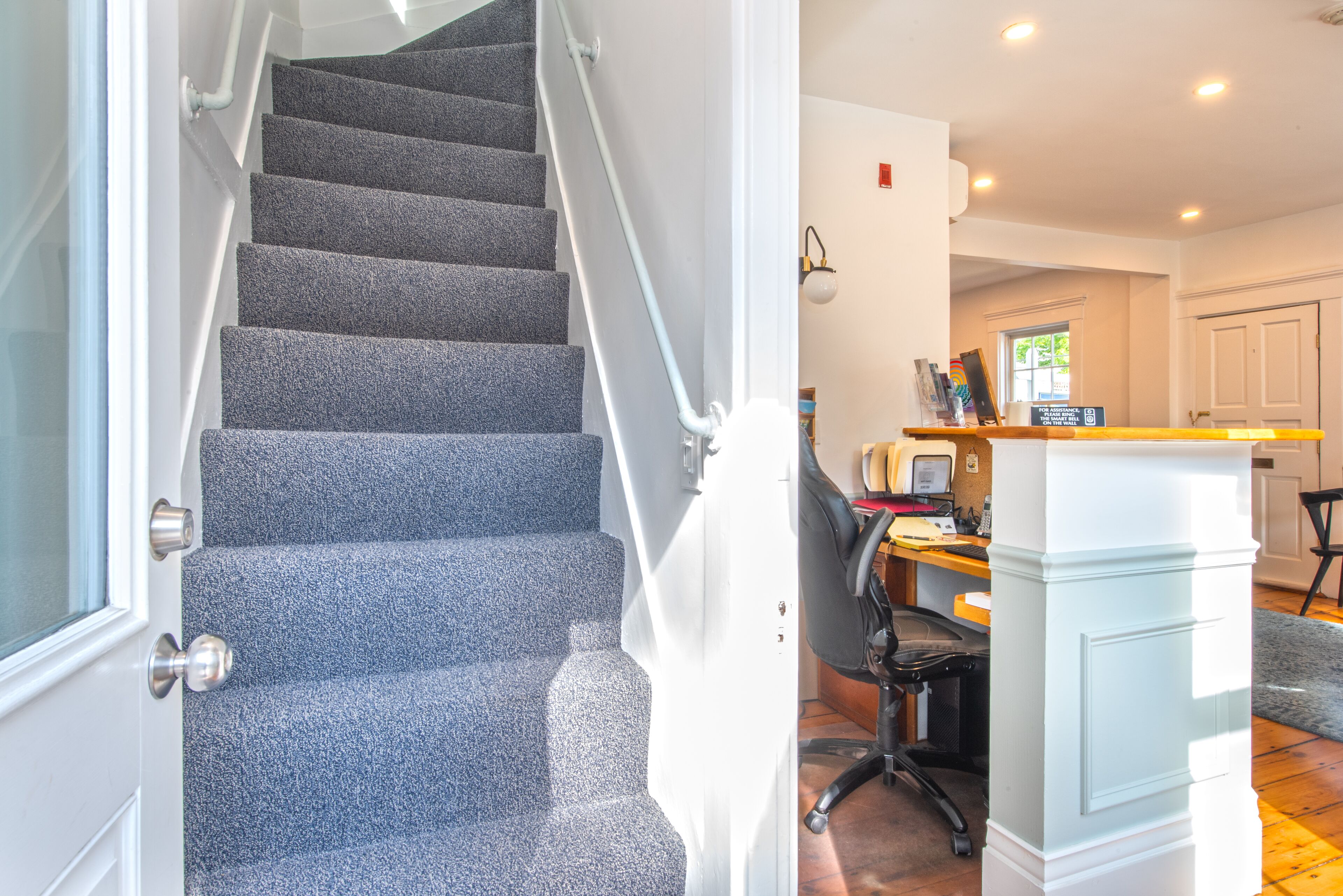 A staircase with carpeted steps leading to a room with a desk, chair, and a computer monitor.