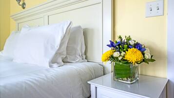 A neatly made bed with white linens and a vase of flowers on a bedside table.