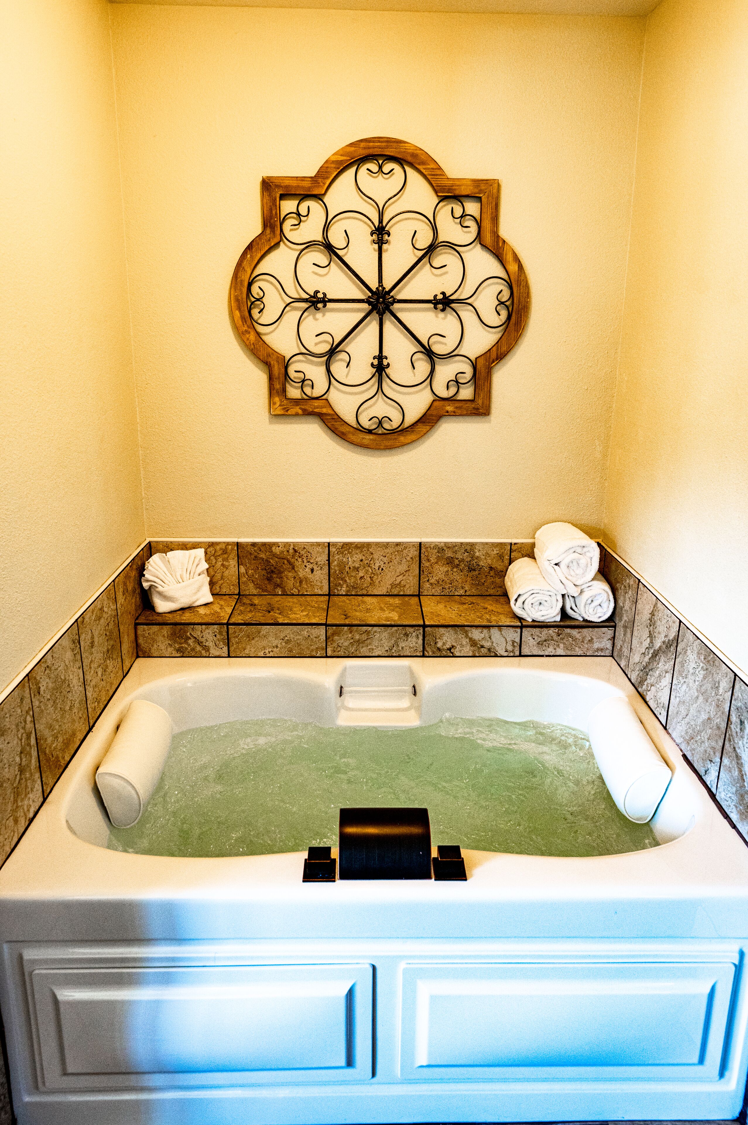 A bathroom with a large bathtub, a decorative wall piece above it, and a towel rack with towels.