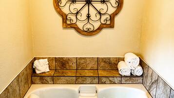 A bathroom with a large bathtub, a decorative wall piece above it, and a towel rack with towels.