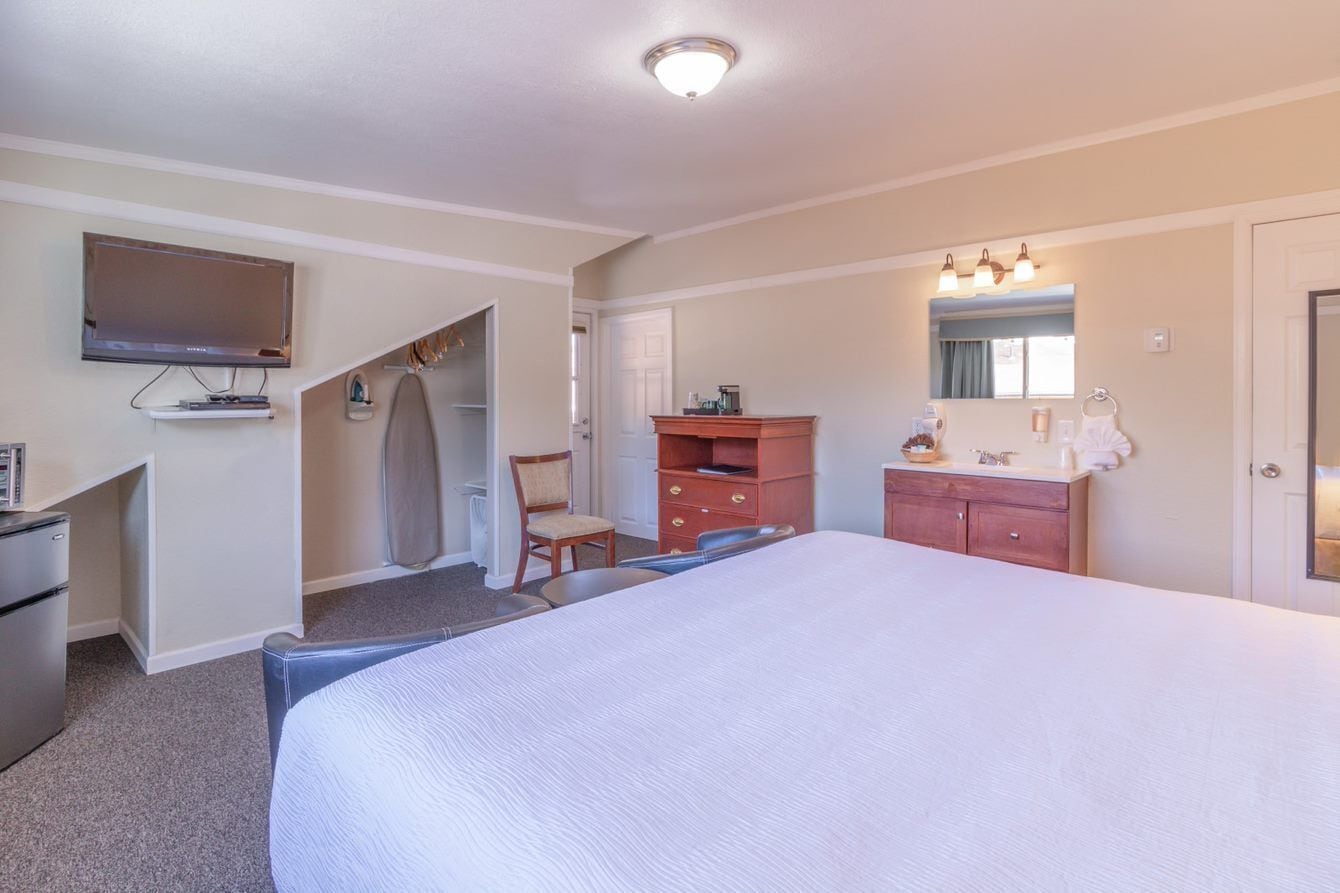 A hotel room with a large bed, a TV mounted on the wall, a desk with a chair, a wardrobe, and a bathroom with a mirror and sink.